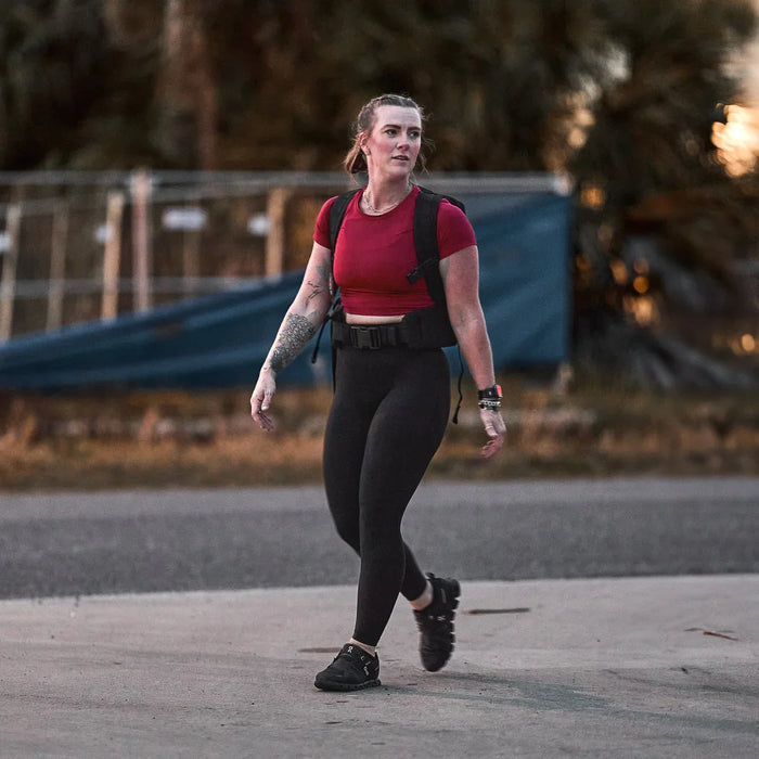 Woman rucking outdoors wearing GORUCK gear, red top, black leggings, rucksack