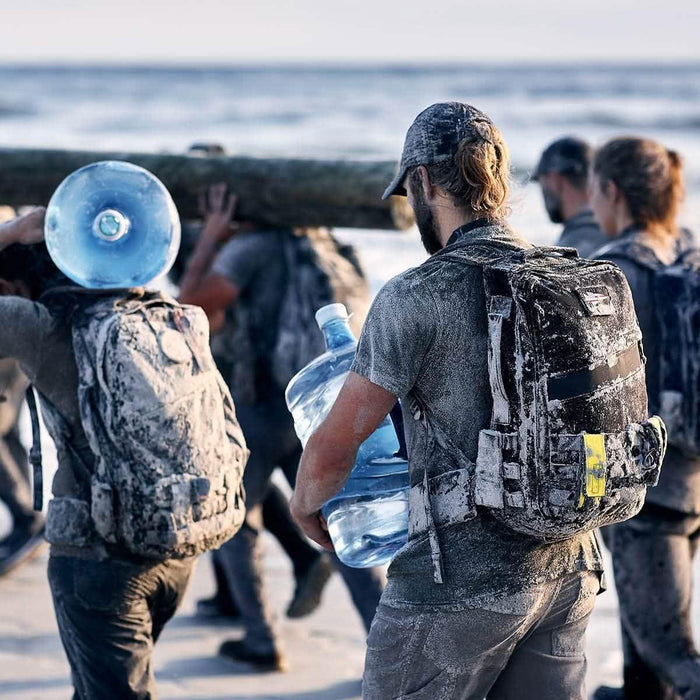 GORUCK rucking gear in use by group on sandy beach, participants carrying heavy loads