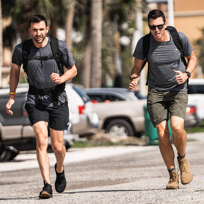 Two men rucking outdoors with GORUCK backpacks and athletic gear in sunny urban setting.