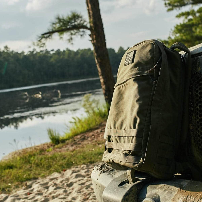 GORUCK tactical backpack with reflective flag patch outdoors by a lake, rugged gear