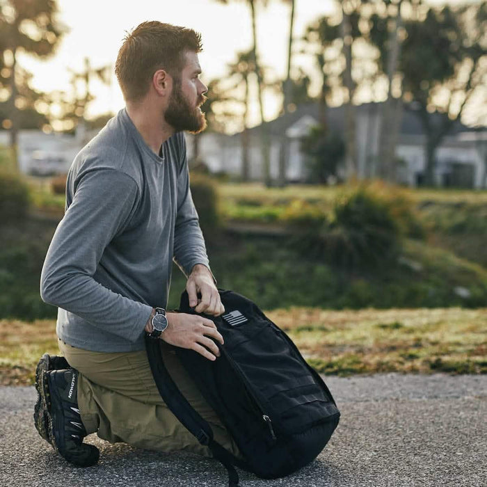 Man kneeling outdoors with a GORUCK black rucksack, preparing for rucking activity