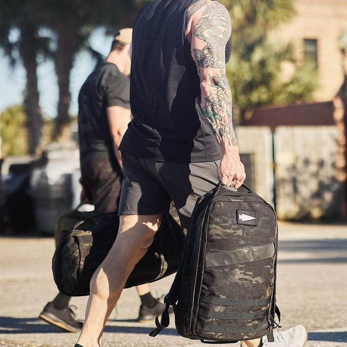 Man carrying GORUCK rucksack outdoors, camo backpack, rucking gear in use