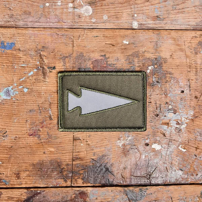 GORUCK reflective green arrowhead patch on distressed wooden surface