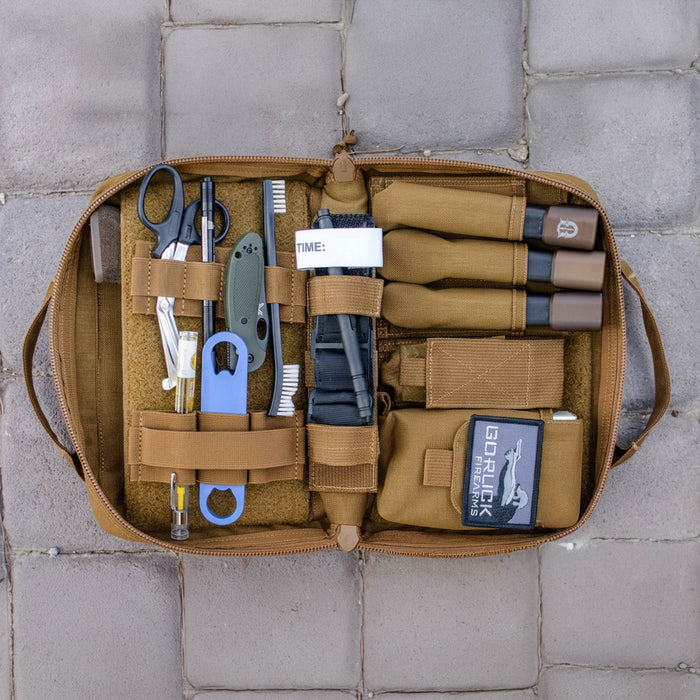 Open tan Pistol Rug with scissors, tools, tourniquets, and supplies neatly organized inside like a modular pistol case, shown on stone tiles.