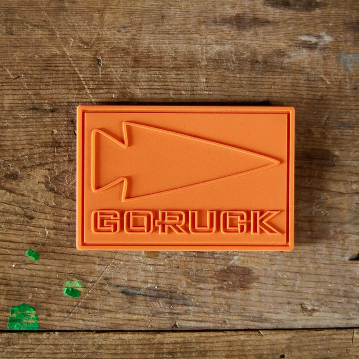 GORUCK orange patch with arrowhead logo on rustic wooden bench
