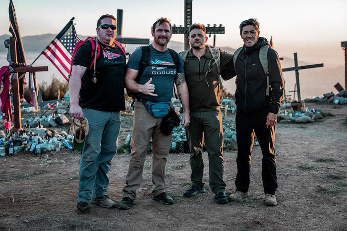 Four men with GORUCK backpacks standing outdoors near crosses and an American flag