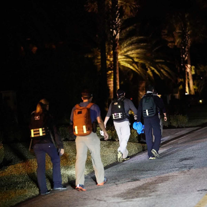 Group wearing GORUCK rucksacks with reflective bands walking at night on a street