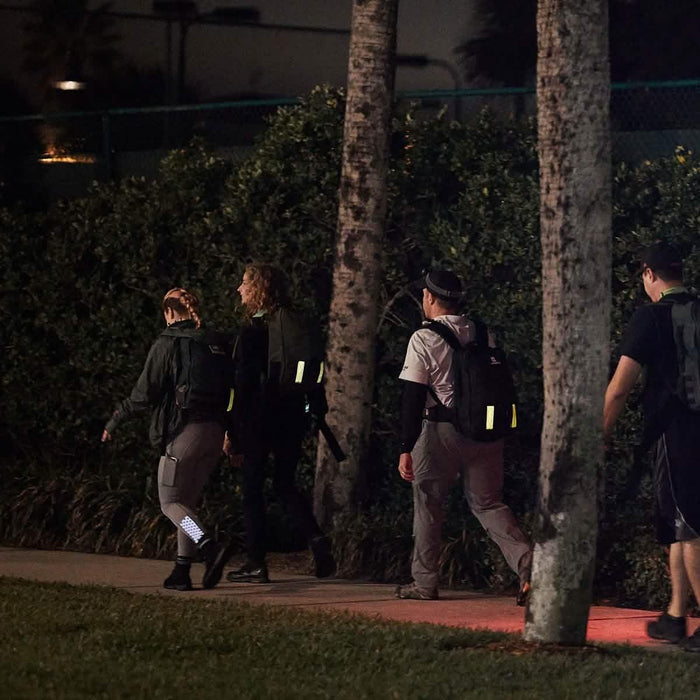 Group using GORUCK rucksacks and reflective bands walking at night outdoors on sidewalk