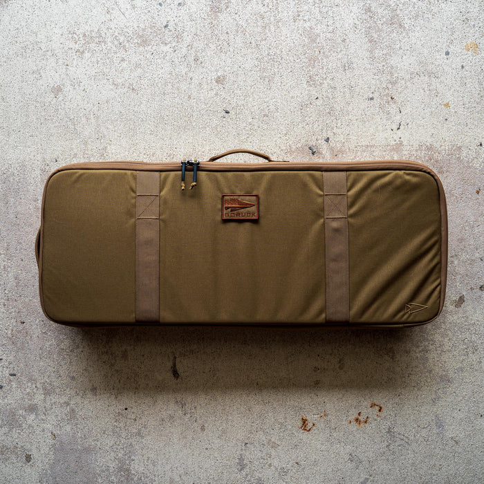 A rectangular brown Rifle Case with handles rests on a speckled concrete floor.