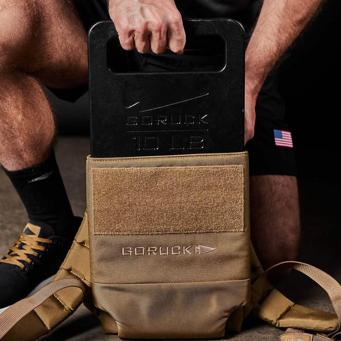 GORUCK 10 lb ruck plate being loaded into tan tactical backpack for rucking fitness