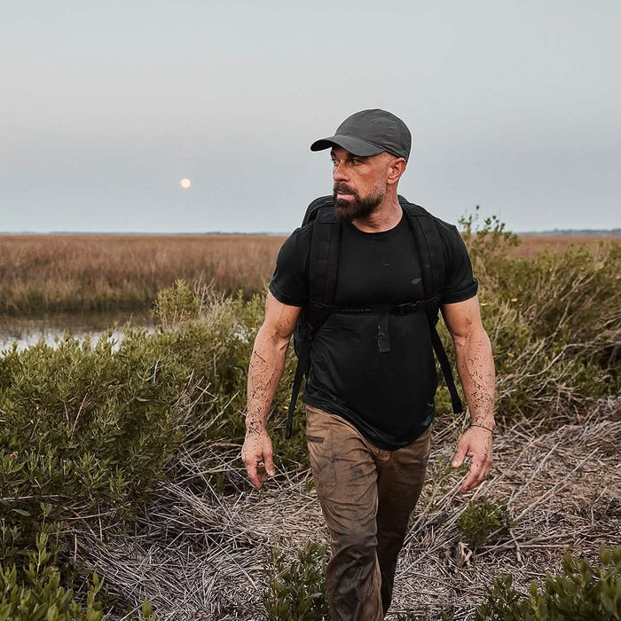 Man with GORUCK rucksack trekking through muddy wilderness at sunset