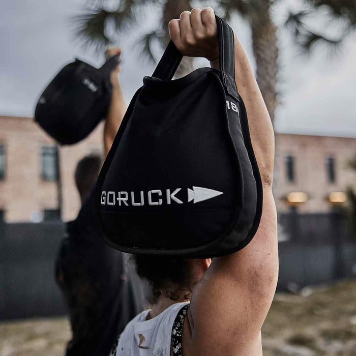 Person lifting GORUCK training sandbag outdoors, showcasing durable rucking gear