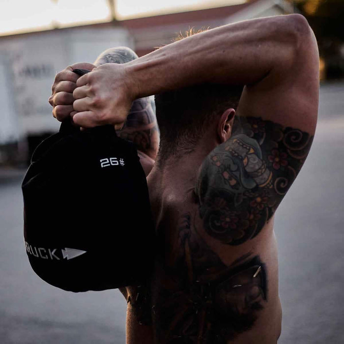 Tattooed man lifting GORUCK 26 lb ruck sandbag outdoors during rucking workout