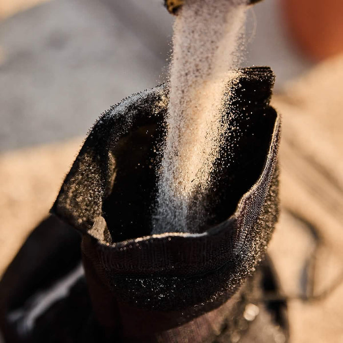 Sand being poured into a durable black GORUCK rucksack sandbag outdoors
