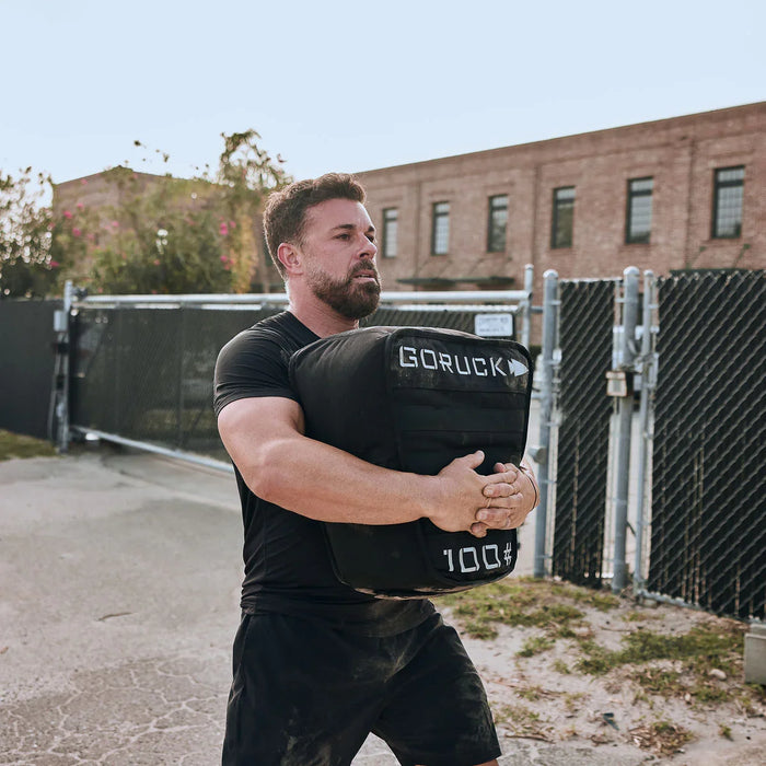 Man lifting GORUCK 100 lb sandbag outdoors, showcasing rucking fitness gear