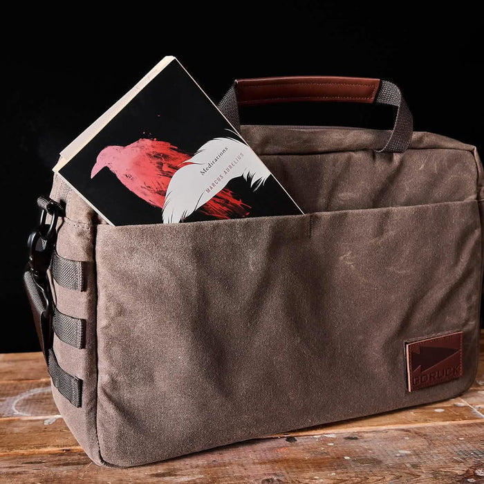GORUCK brown canvas bag on wood table with book in front pocket, rugged rucking gear