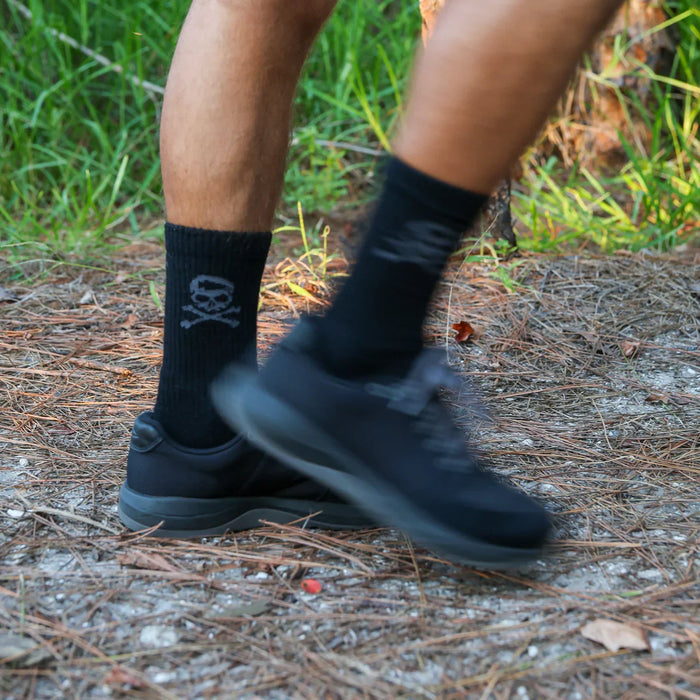 Person rucking on a forest trail wearing GORUCK black shoes and skull logo socks