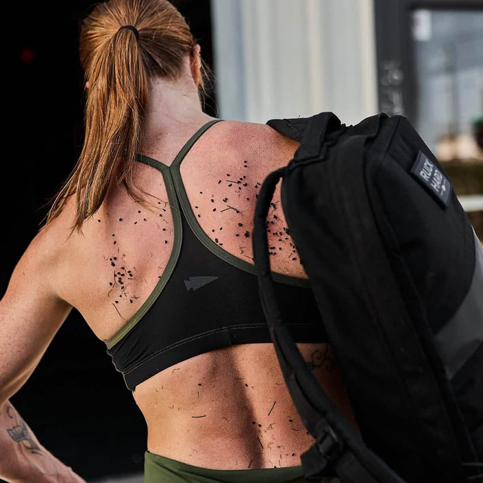 Woman with brown hair wearing a GORUCK rucksack, in athletic gear with grass on her back.