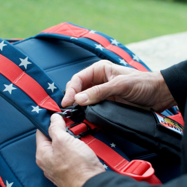 Hands adjusting the strap on a blue backpack with red, star-patterned straps, featuring a Sternum Pouch - Cordura attached for extra storage.