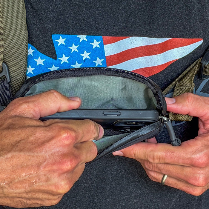 Hands placing a smartphone into the Sternum / Belt Pouch - Waterproof X-PAC for convenient access, with an American flag shirt in the background.