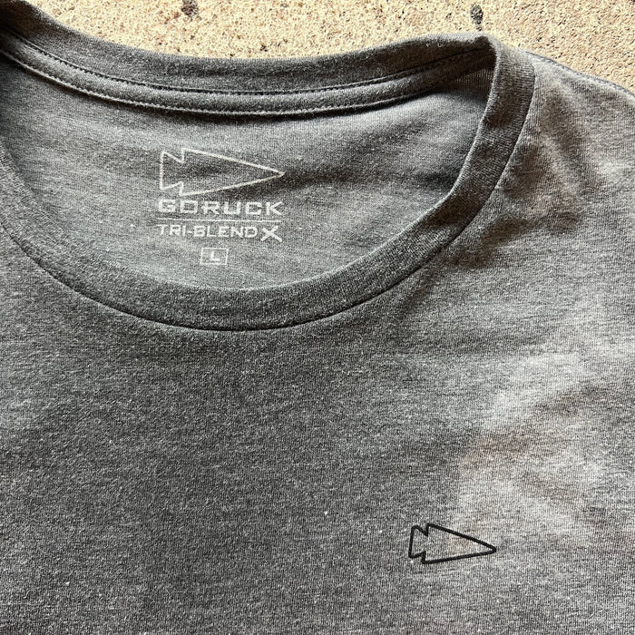 The Subtle Spearhead Tee - Unisex Tri-Blend is a gray t-shirt with a small arrow logo on the chest and inside the collar, inspired by Special Forces and featuring Anti-Stink technology.