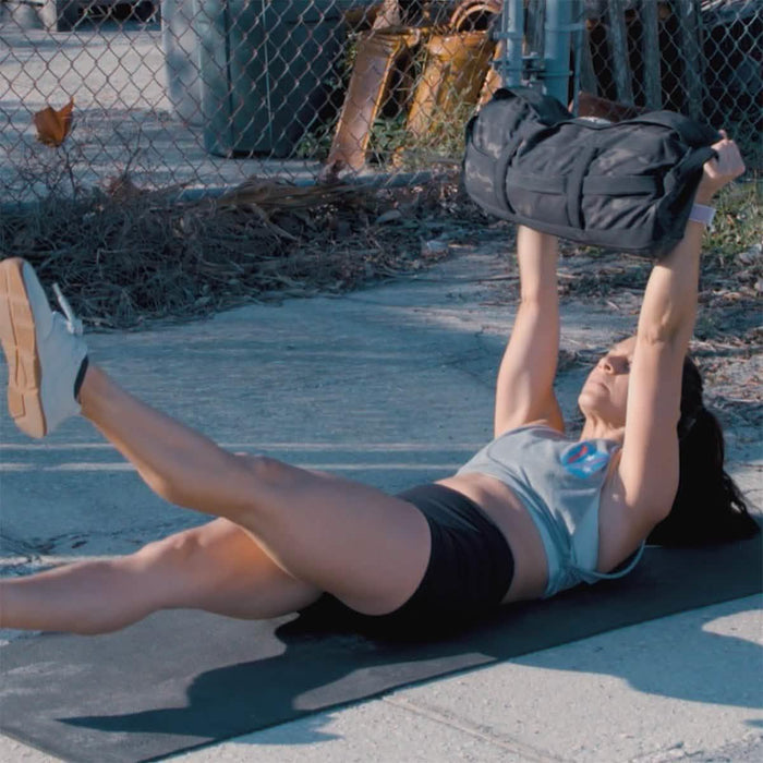 Woman doing rucking workout with GORUCK sandbag outdoors on exercise mat