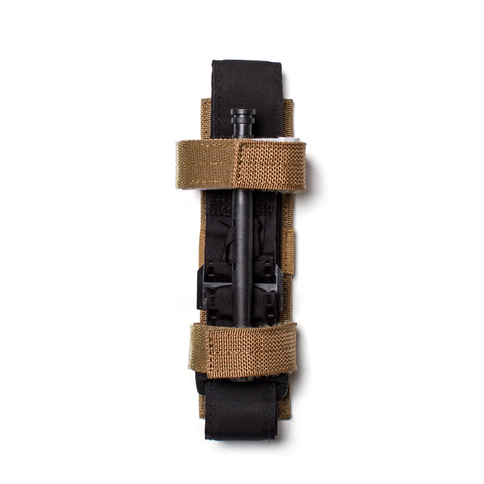A Tourniquet Attachment in black, fastened with two tan hook-and-loop retention straps, is photographed on a white background from a top view.