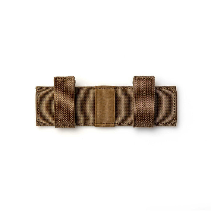 The Tourniquet Attachment is a brown nylon strap with two loops and reinforced stitching, designed as a compact book-style organizer, shown laid flat on a white background.