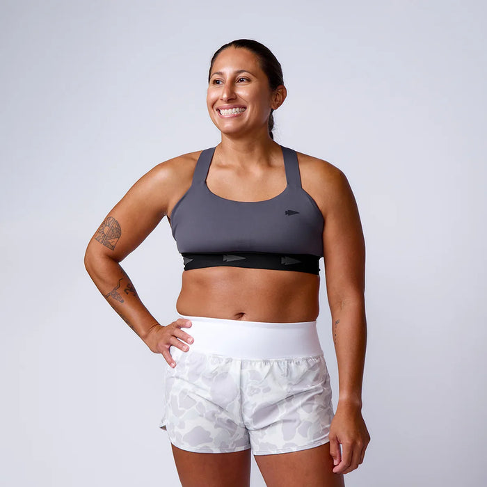 Woman in GORUCK athletic gear, gray sports bra and white camo shorts, studio background