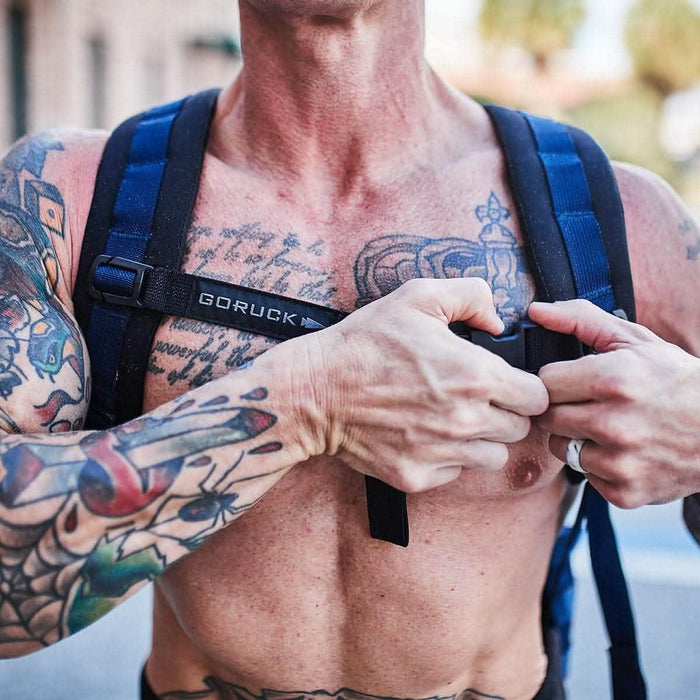 Tattooed person adjusting GORUCK backpack sternum strap outdoors, close-up view