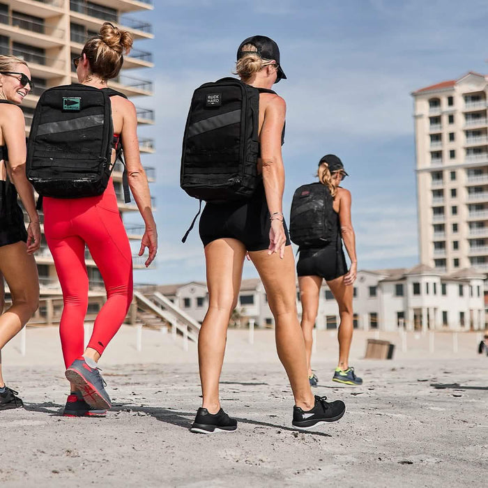 Women rucking on beach wearing GORUCK backpacks, athletic apparel, and sneakers.