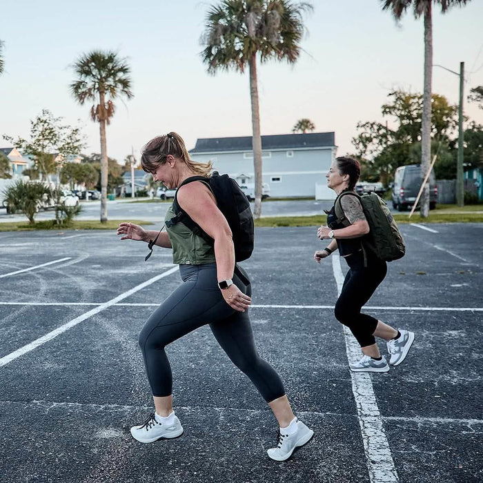 Two women rucking in GORUCK ballistic trainers with backpacks in a parking lot