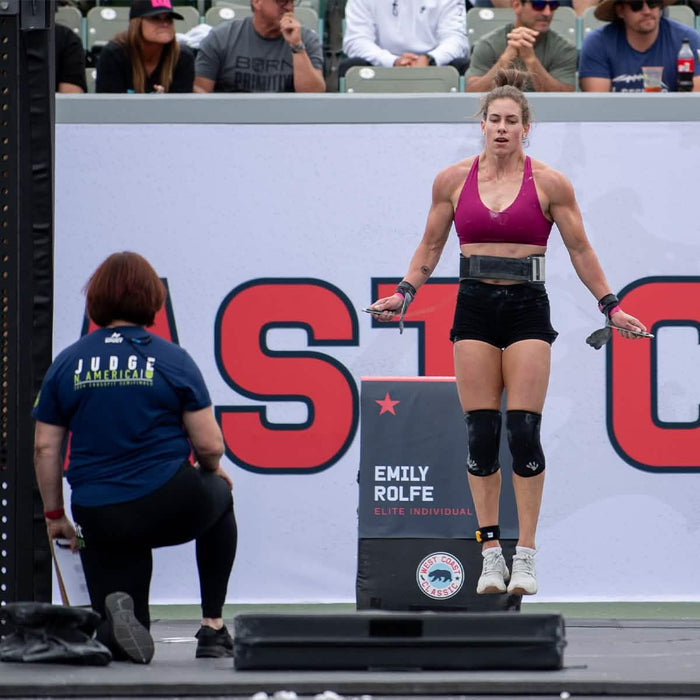 Female athlete performing jump rope at CrossFit event with judge and spectators