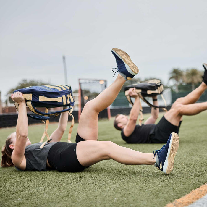Two people rucking with GORUCK sandbags while exercising on a turf field outdoors