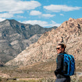 Woman hiking with blue GORUCK backpack in rugged mountain landscape, outdoor adventure gear