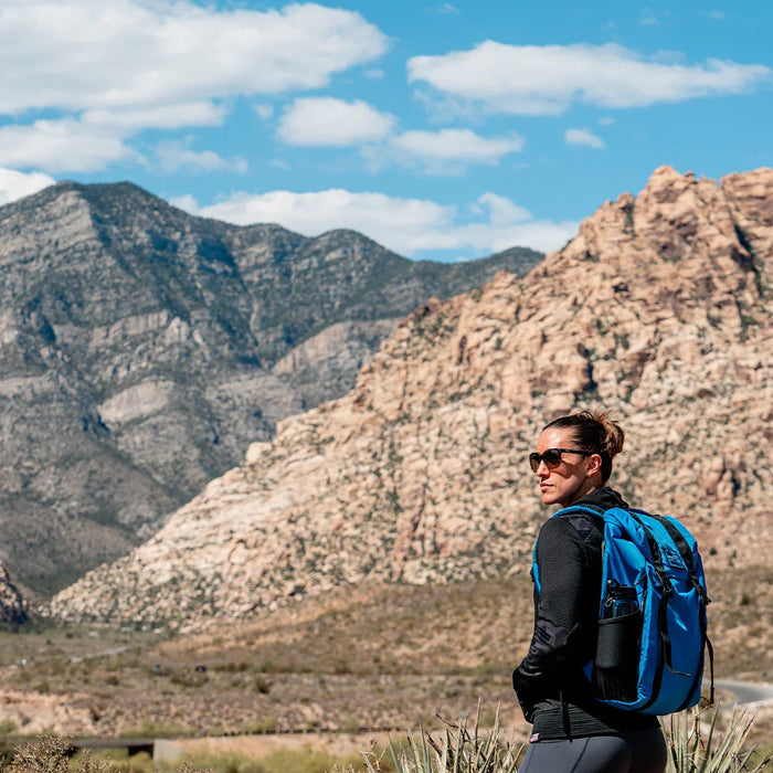 Woman hiking with blue GORUCK backpack in rugged mountain landscape, outdoor adventure gear