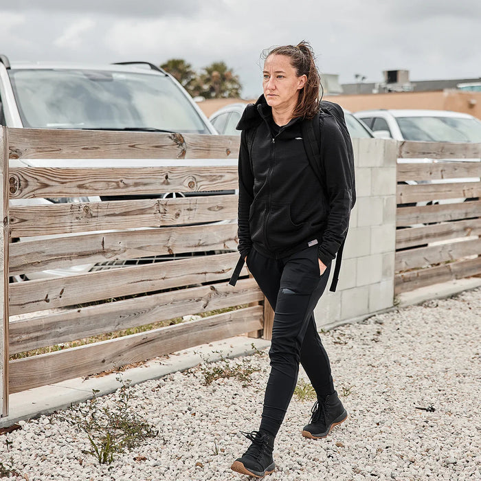 Woman in black GORUCK fleece hoodie and joggers walking outdoors with a rucksack