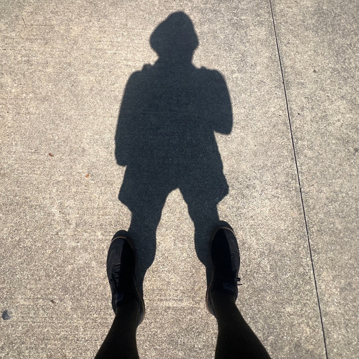 Shadow of a person wearing shorts, shoes, and the Men's USA Sun Hoodie - Full-Zip - ToughMesh, with their feet visible at the bottom, cast on the pavement.