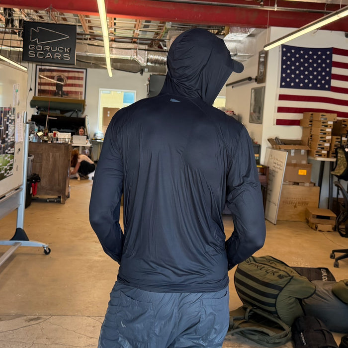 A person wearing the Men's USA Sun Hoodie - Full-Zip - ToughMesh stands in a room with American flags and gear in the background.