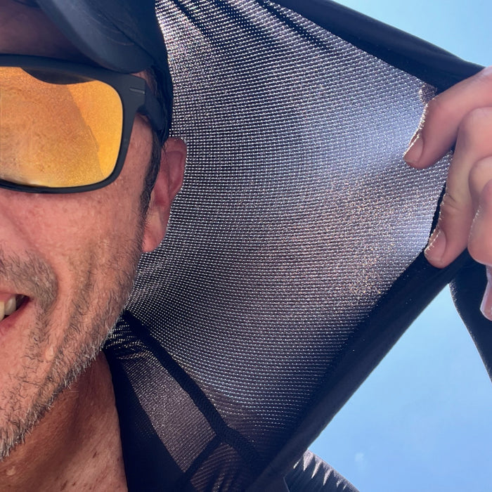 A man in a hat and sunglasses holds up the Men's USA Sun Hoodie - Full-Zip - ToughMesh against bright sunlight, blue sky behind him.