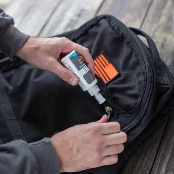 Applying zipper lubricant to GORUCK backpack zipper on wooden surface